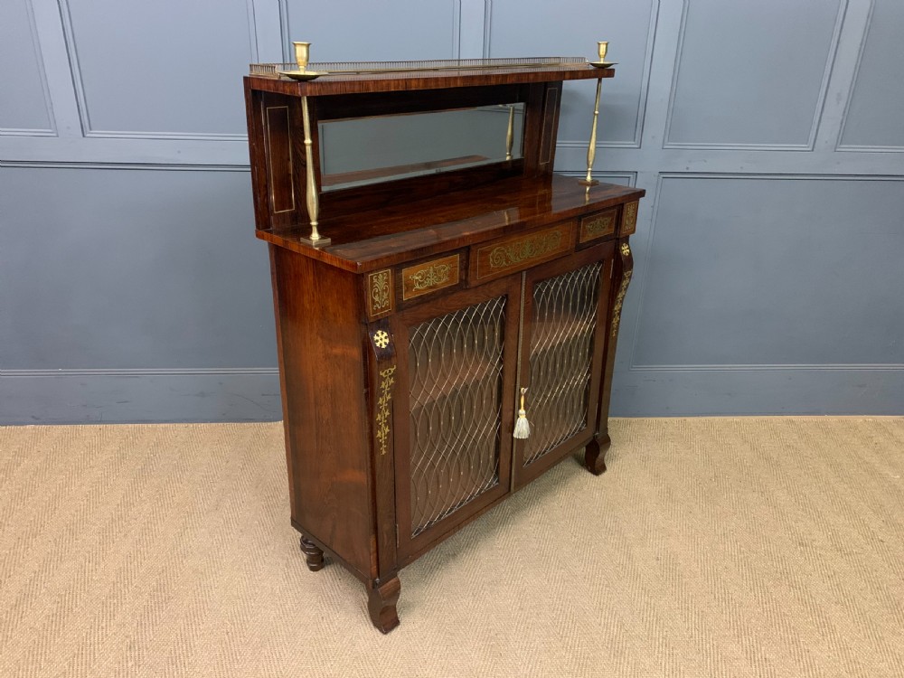 An antique Regency rosewood chiffonier featuring ornate brass inlay, a top mirror back with a brass gallery rail, and twin doors with brass wire mesh. View XV