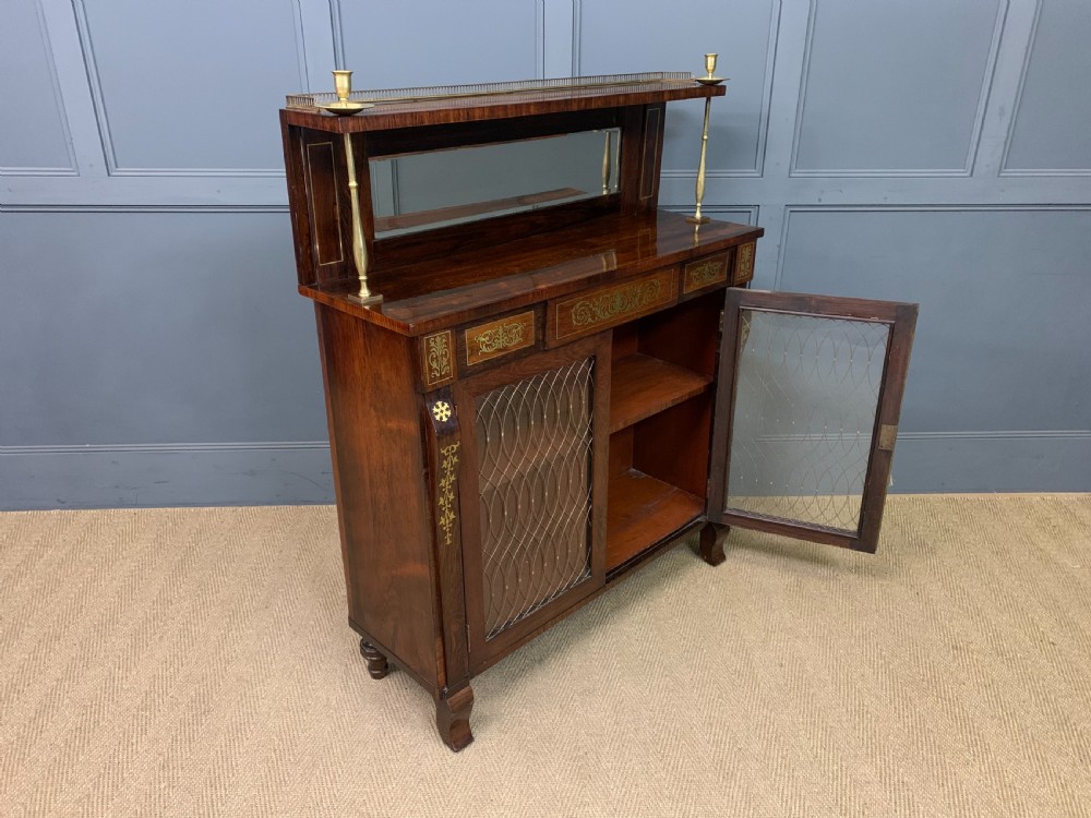 An antique Regency rosewood chiffonier featuring ornate brass inlay, a top mirror back with a brass gallery rail, and twin doors with brass wire mesh. View XVII