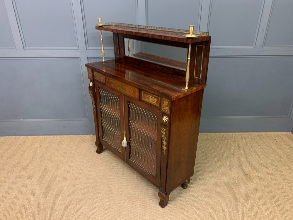 An antique Regency rosewood chiffonier featuring ornate brass inlay, a top mirror back with a brass gallery rail, and twin doors with brass wire mesh. View XVIII