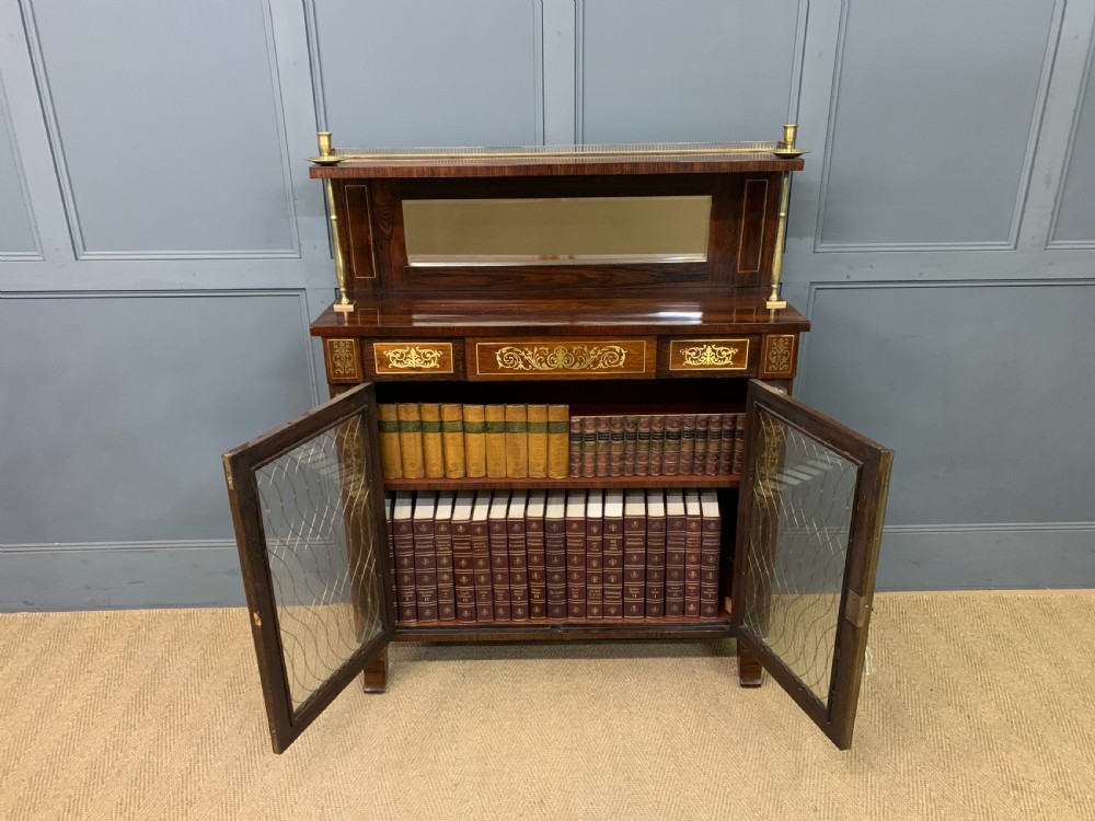 An antique Regency rosewood chiffonier featuring ornate brass inlay, a top mirror back with a brass gallery rail, and twin doors with brass wire mesh. View XXIII