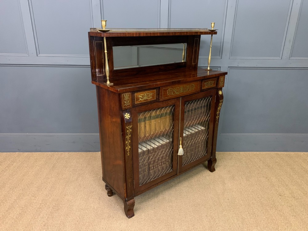 An antique Regency rosewood chiffonier featuring ornate brass inlay, a top mirror back with a brass gallery rail, and twin doors with brass wire mesh. View XXVI
