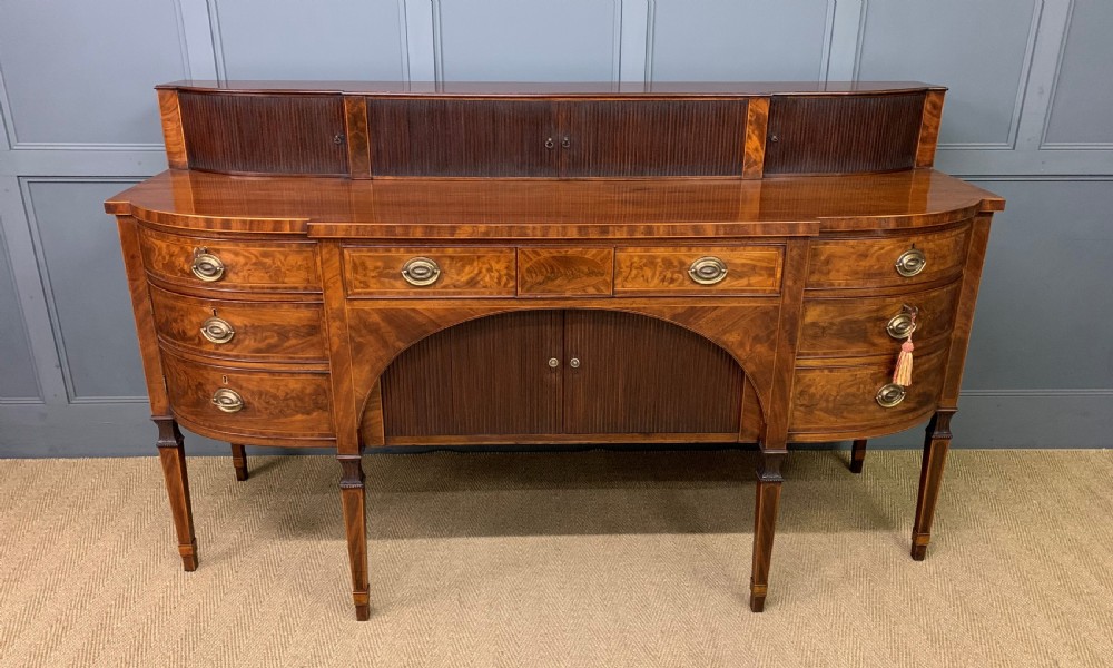 An antique George III inlaid mahogany sideboard with flame wood veneers, tambour doors, and brass ring drawer handles.