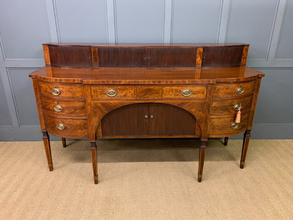 An antique George III inlaid mahogany sideboard with flame wood veneers, tambour doors, and brass ring drawer handles. View II