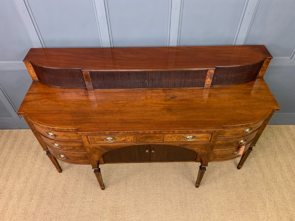 An antique George III inlaid mahogany sideboard with flame wood veneers, tambour doors, and brass ring drawer handles. View IV