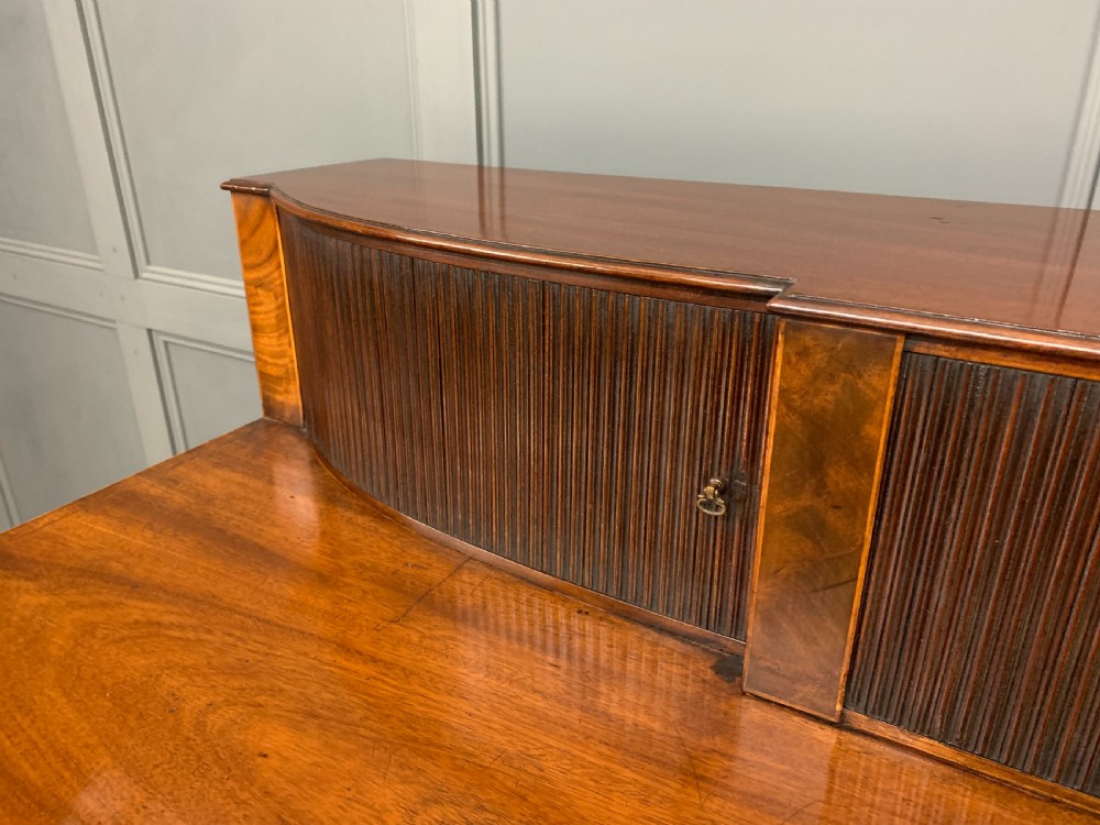 An antique George III inlaid mahogany sideboard with flame wood veneers, tambour doors, and brass ring drawer handles. View V