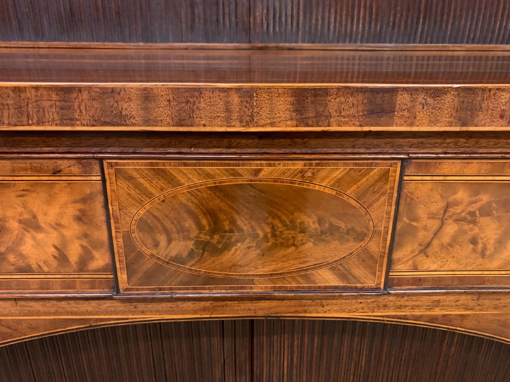 An antique George III inlaid mahogany sideboard with flame wood veneers, tambour doors, and brass ring drawer handles. View X