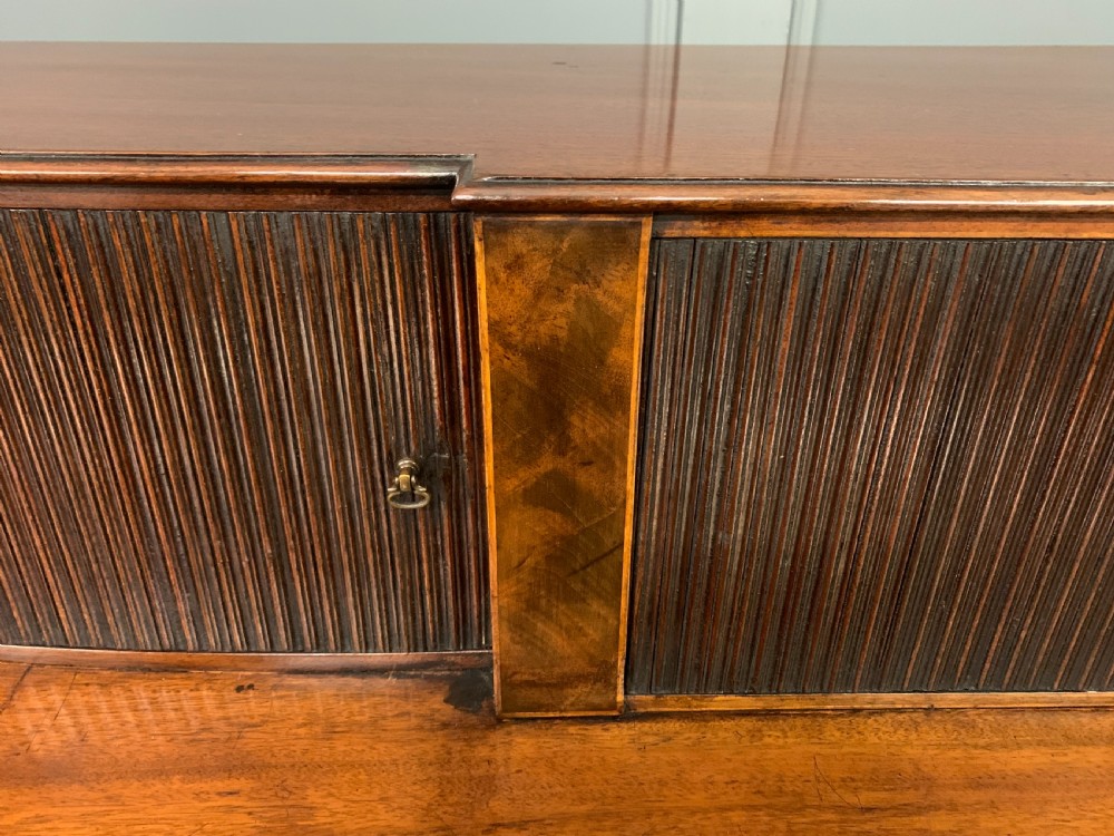 An antique George III inlaid mahogany sideboard with flame wood veneers, tambour doors, and brass ring drawer handles. View XII
