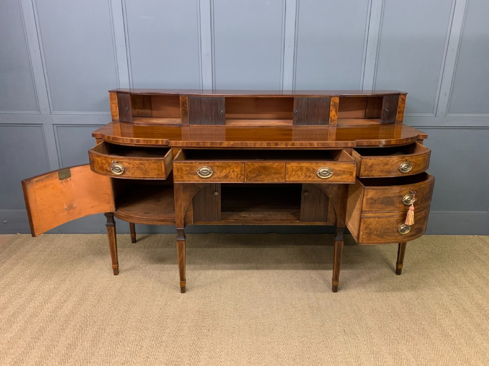 An antique George III inlaid mahogany sideboard with flame wood veneers, tambour doors, and brass ring drawer handles. View XIII