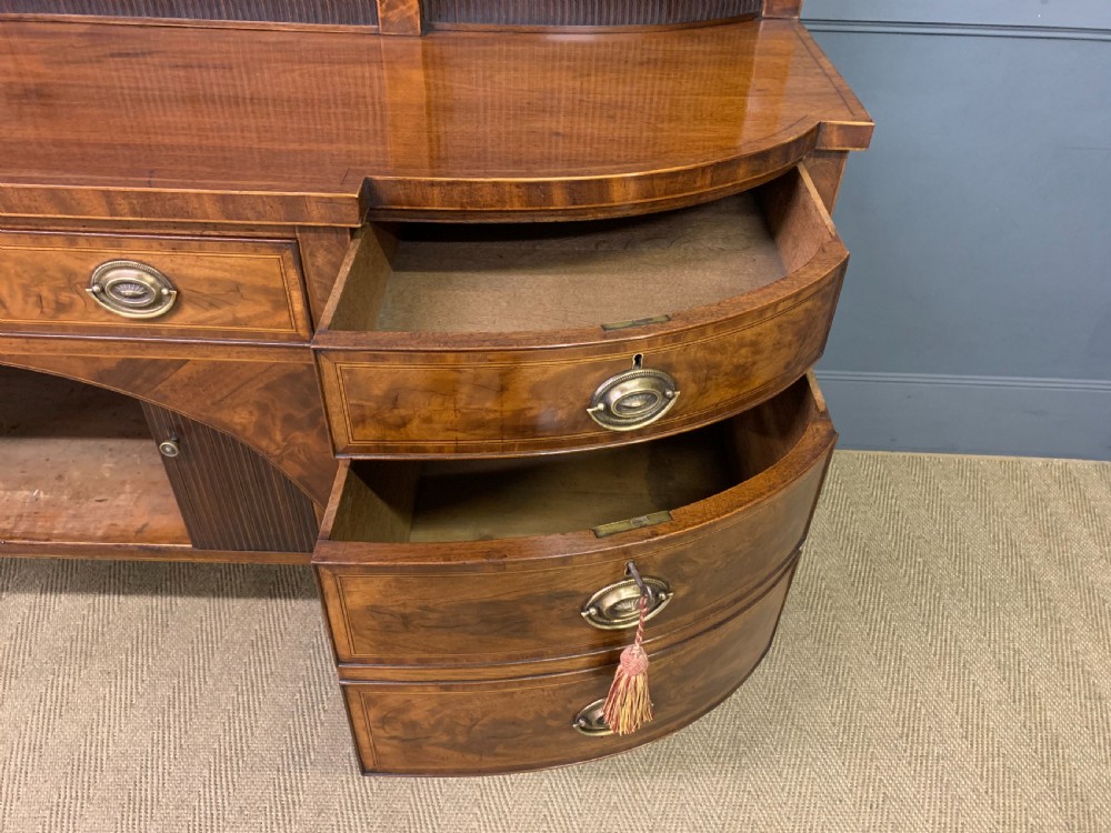 An antique George III inlaid mahogany sideboard with flame wood veneers, tambour doors, and brass ring drawer handles. View XVI