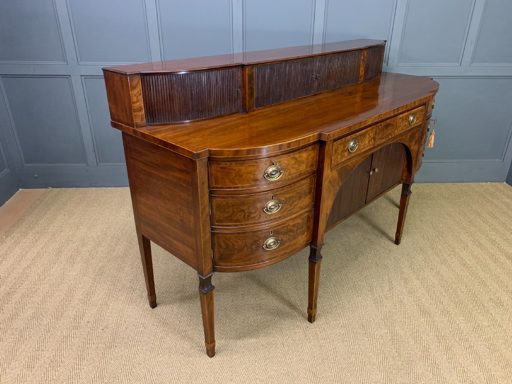 An antique George III inlaid mahogany sideboard with flame wood veneers, tambour doors, and brass ring drawer handles. View XVIII