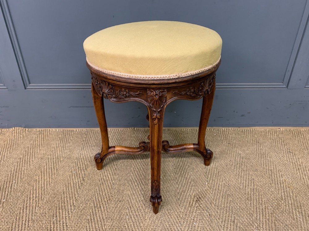 A French carved walnut adjustable piano stool with cabriole legs, carved floral apron, X-shaped stretcher, and a round light yellow upholstered seat. View IV