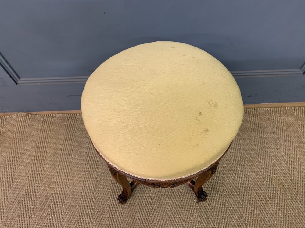 A French carved walnut adjustable piano stool with cabriole legs, carved floral apron, X-shaped stretcher, and a round light yellow upholstered seat. View V