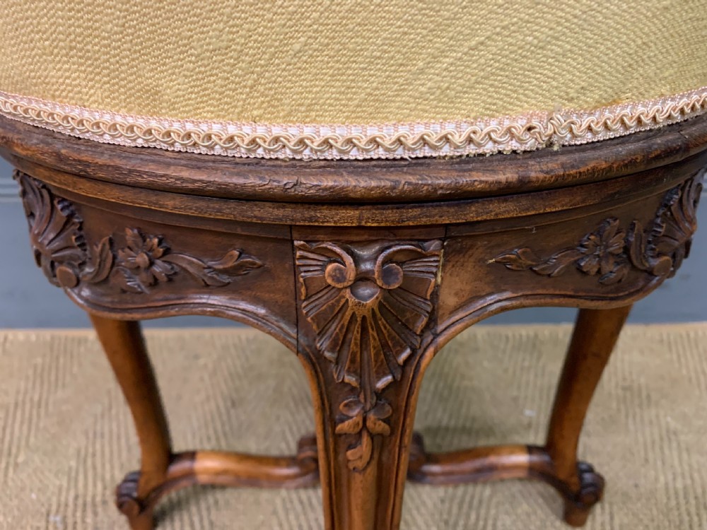 A French carved walnut adjustable piano stool with cabriole legs, carved floral apron, X-shaped stretcher, and a round light yellow upholstered seat. View VII