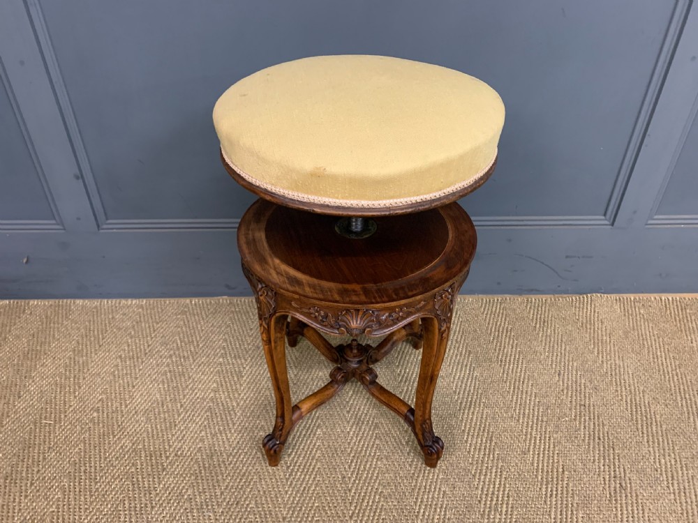 A French carved walnut adjustable piano stool with cabriole legs, carved floral apron, X-shaped stretcher, and a round light yellow upholstered seat. View VIII