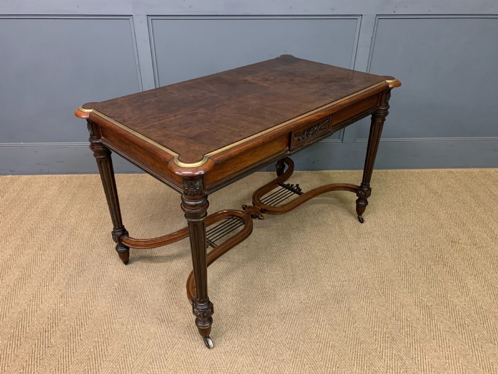 A rectangular French mahogany library table featuring a polished top, frieze drawer with carved detail, brass trim, turned fluted legs, and a lower carved stretcher on brass castors.