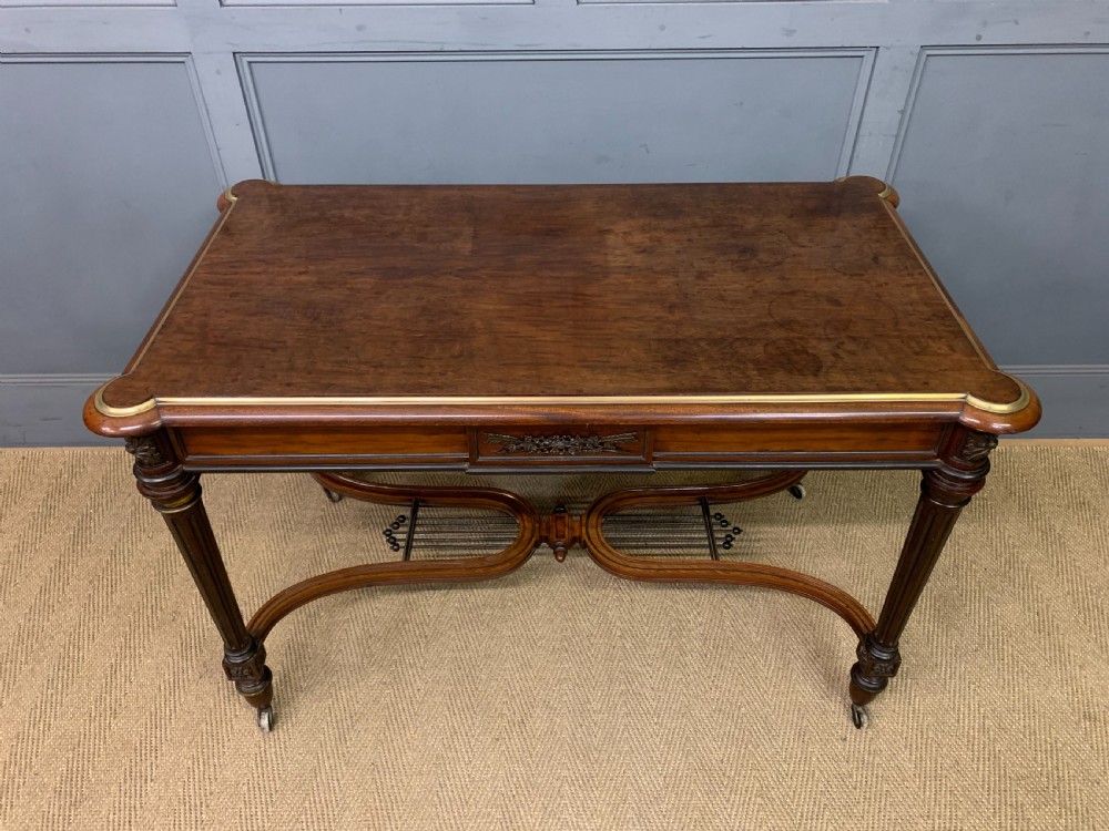 A rectangular French mahogany library table featuring a polished top, frieze drawer with carved detail, brass trim, turned fluted legs, and a lower carved stretcher on brass castors. View III