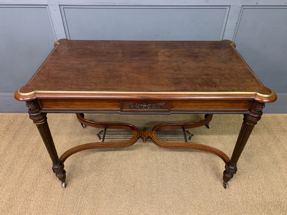 A rectangular French mahogany library table featuring a polished top, frieze drawer with carved detail, brass trim, turned fluted legs, and a lower carved stretcher on brass castors. View IV