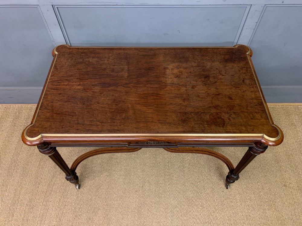 A rectangular French mahogany library table featuring a polished top, frieze drawer with carved detail, brass trim, turned fluted legs, and a lower carved stretcher on brass castors. View V