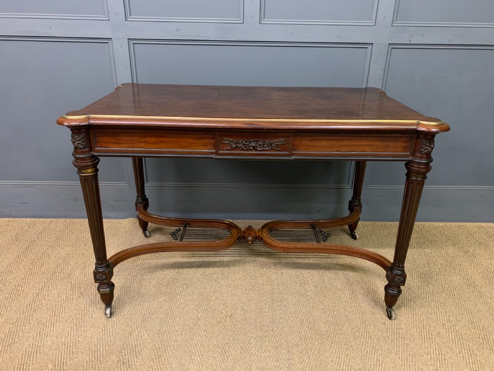 A rectangular French mahogany library table featuring a polished top, frieze drawer with carved detail, brass trim, turned fluted legs, and a lower carved stretcher on brass castors. View VI