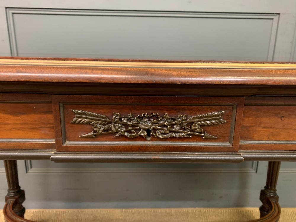 A rectangular French mahogany library table featuring a polished top, frieze drawer with carved detail, brass trim, turned fluted legs, and a lower carved stretcher on brass castors. View VII