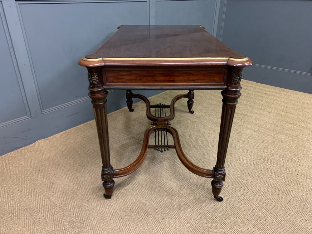 A rectangular French mahogany library table featuring a polished top, frieze drawer with carved detail, brass trim, turned fluted legs, and a lower carved stretcher on brass castors. View XIII