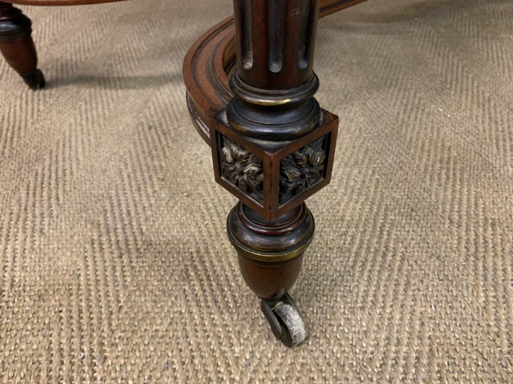 A rectangular French mahogany library table featuring a polished top, frieze drawer with carved detail, brass trim, turned fluted legs, and a lower carved stretcher on brass castors. View XV