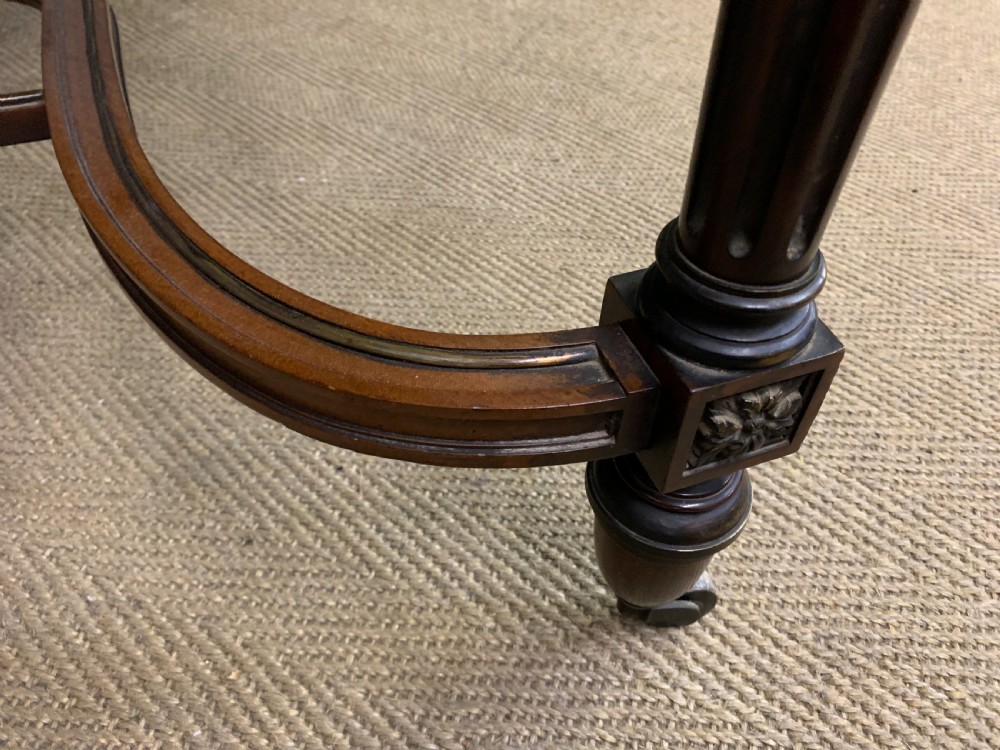 A rectangular French mahogany library table featuring a polished top, frieze drawer with carved detail, brass trim, turned fluted legs, and a lower carved stretcher on brass castors. View XVI