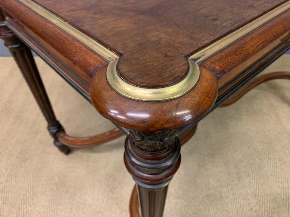 A rectangular French mahogany library table featuring a polished top, frieze drawer with carved detail, brass trim, turned fluted legs, and a lower carved stretcher on brass castors. View XVIII