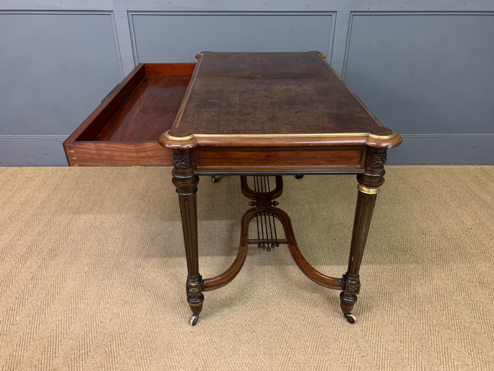 A rectangular French mahogany library table featuring a polished top, frieze drawer with carved detail, brass trim, turned fluted legs, and a lower carved stretcher on brass castors. View XXI
