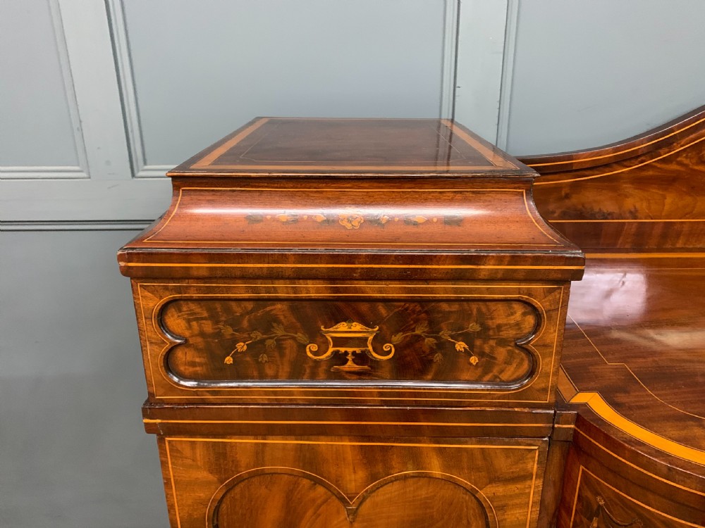 A George III inlaid mahogany pedestal sideboard featuring twin cupboard pedestals decorated with urn marquetry and a shaped backboard. View II