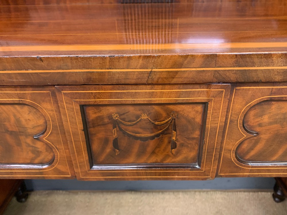 A George III inlaid mahogany pedestal sideboard featuring twin cupboard pedestals decorated with urn marquetry and a shaped backboard. View X