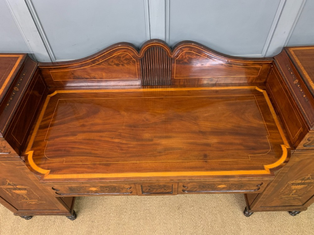A George III inlaid mahogany pedestal sideboard featuring twin cupboard pedestals decorated with urn marquetry and a shaped backboard. View XIV