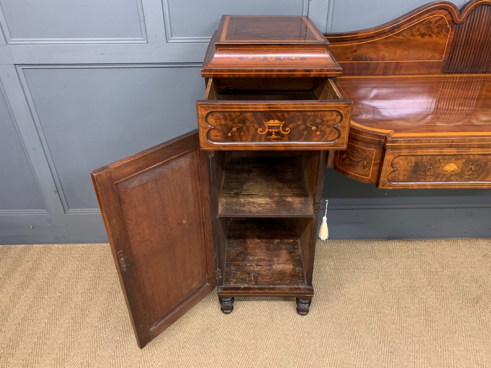 A George III inlaid mahogany pedestal sideboard featuring twin cupboard pedestals decorated with urn marquetry and a shaped backboard. View XVI