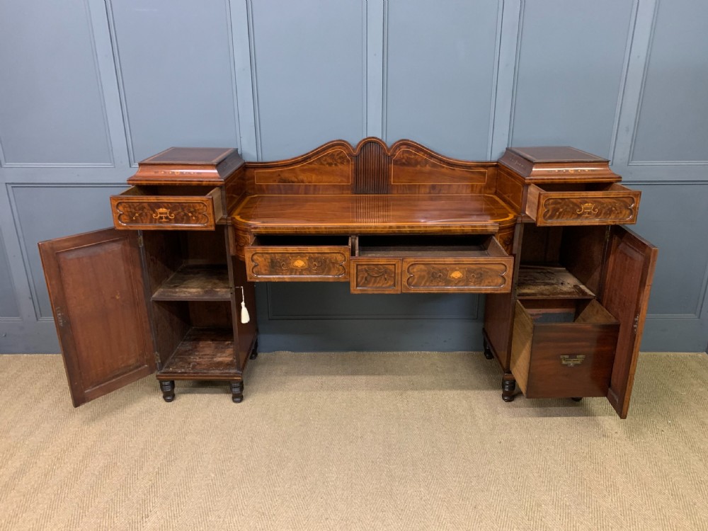 A George III inlaid mahogany pedestal sideboard featuring twin cupboard pedestals decorated with urn marquetry and a shaped backboard. View XVII