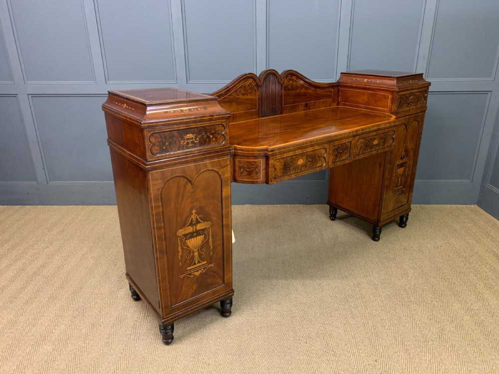 A George III inlaid mahogany pedestal sideboard featuring twin cupboard pedestals decorated with urn marquetry and a shaped backboard. View XX