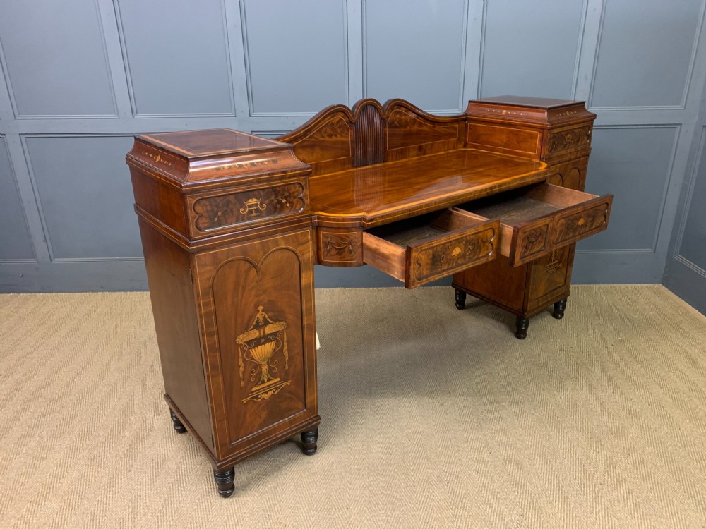 A George III inlaid mahogany pedestal sideboard featuring twin cupboard pedestals decorated with urn marquetry and a shaped backboard. View XXII