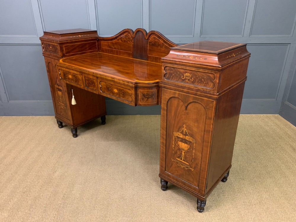 A George III inlaid mahogany pedestal sideboard featuring twin cupboard pedestals decorated with urn marquetry and a shaped backboard. View XXIII