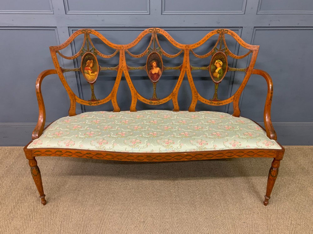 A painted satinwood three-seat settee with central portrait medallions and a light green floral upholstered cushion.