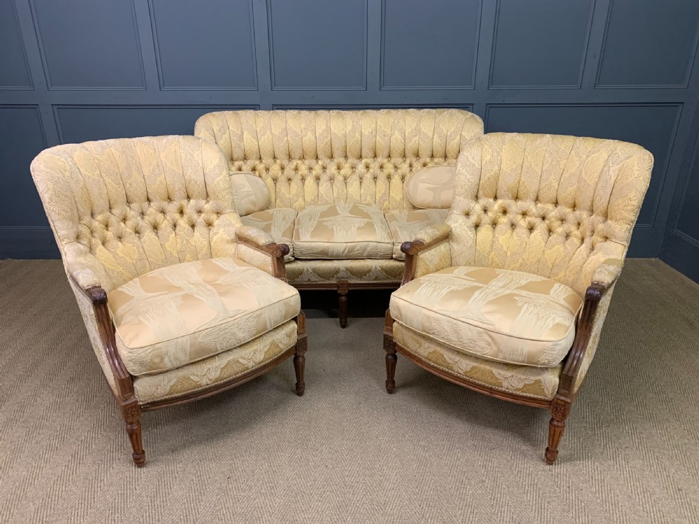 A three-piece French walnut salon suite featuring a sofa and two matching armchairs upholstered in gold patterned damask with deep buttoned backrests and fluted carved legs.