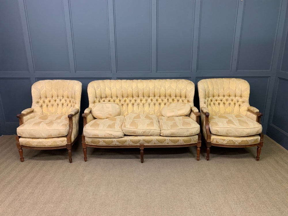 A three-piece French walnut salon suite featuring a sofa and two matching armchairs upholstered in gold patterned damask with deep buttoned backrests and fluted carved legs. View II