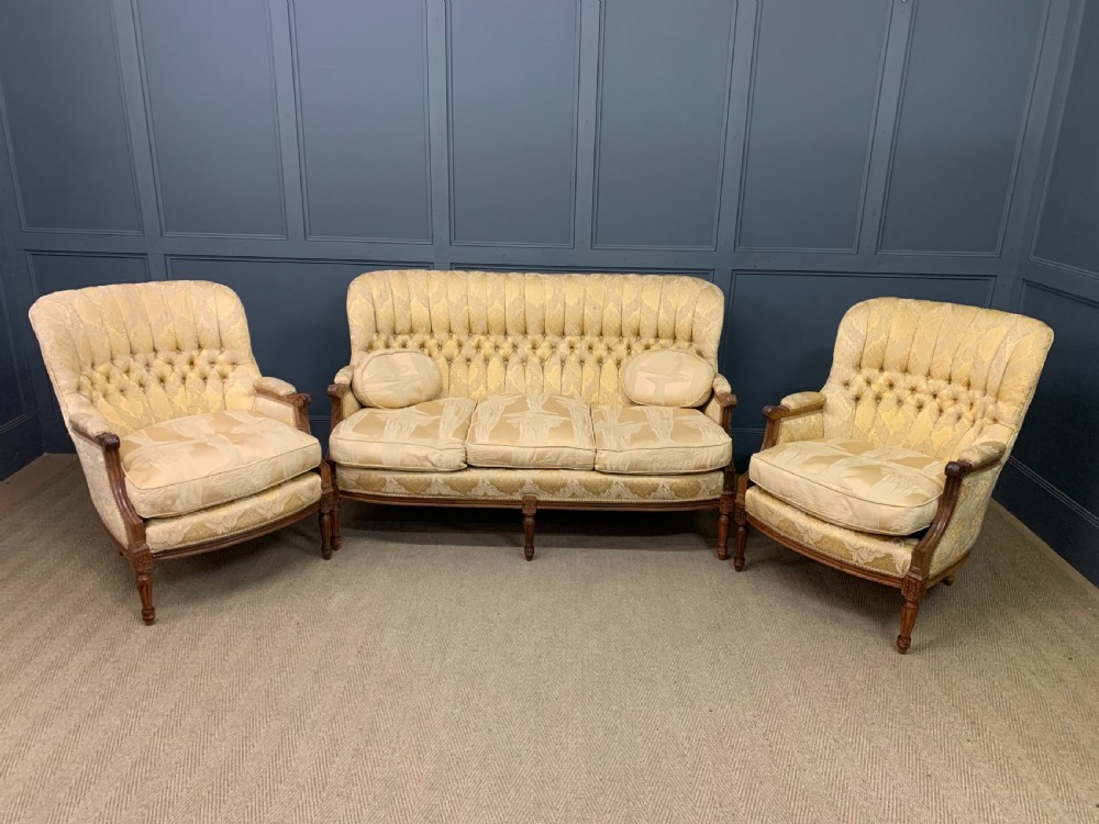 A three-piece French walnut salon suite featuring a sofa and two matching armchairs upholstered in gold patterned damask with deep buttoned backrests and fluted carved legs. View III