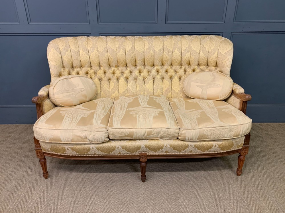 A three-piece French walnut salon suite featuring a sofa and two matching armchairs upholstered in gold patterned damask with deep buttoned backrests and fluted carved legs. View IV