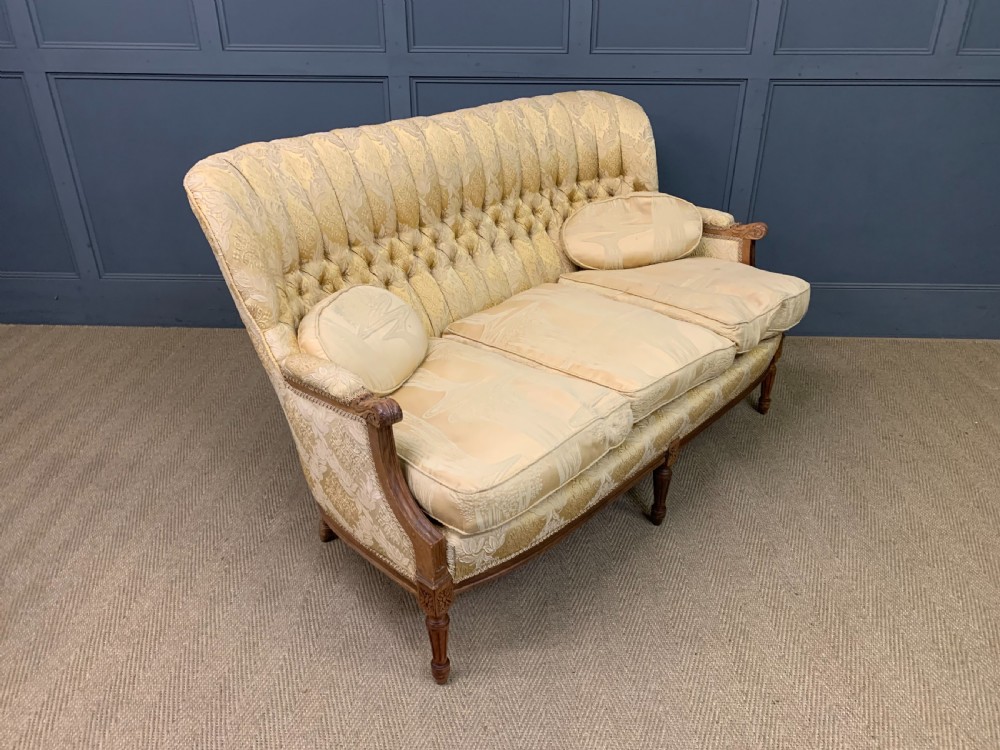 A three-piece French walnut salon suite featuring a sofa and two matching armchairs upholstered in gold patterned damask with deep buttoned backrests and fluted carved legs. View X