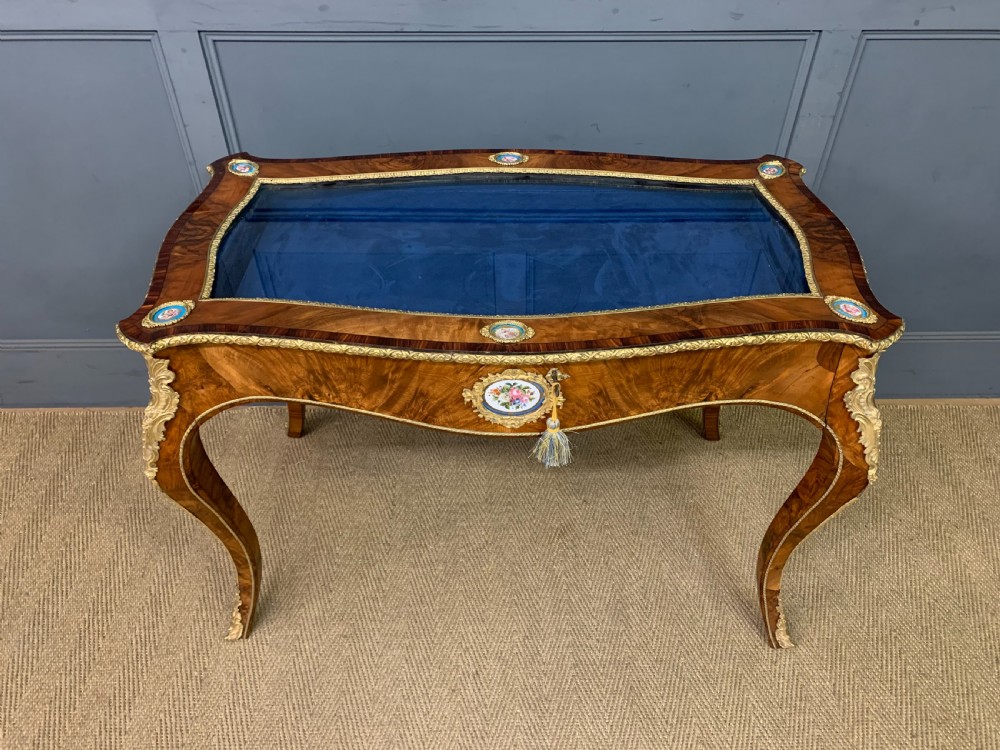 A 19th-century French Louis XV style bijouterie table with a glazed display top, curved cabriole legs, gilt bronze mounts, porcelain plaques, and a blue velvet interior. View IV