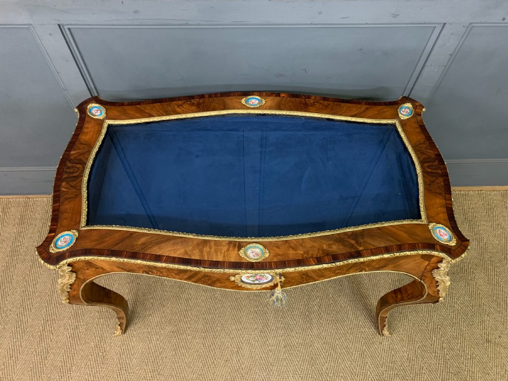 A 19th-century French Louis XV style bijouterie table with a glazed display top, curved cabriole legs, gilt bronze mounts, porcelain plaques, and a blue velvet interior. View V
