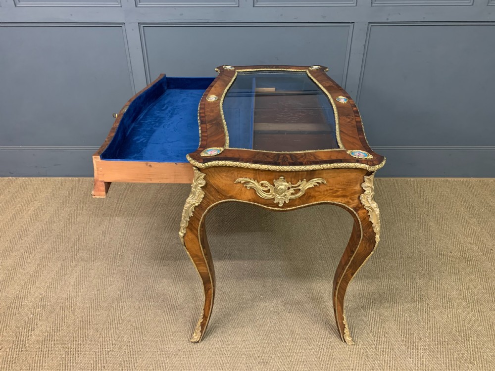 A 19th-century French Louis XV style bijouterie table with a glazed display top, curved cabriole legs, gilt bronze mounts, porcelain plaques, and a blue velvet interior. View XVII