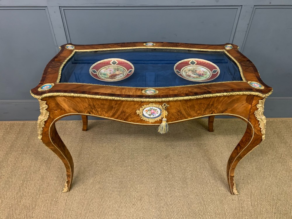 A 19th-century French Louis XV style bijouterie table with a glazed display top, curved cabriole legs, gilt bronze mounts, porcelain plaques, and a blue velvet interior. View XIX