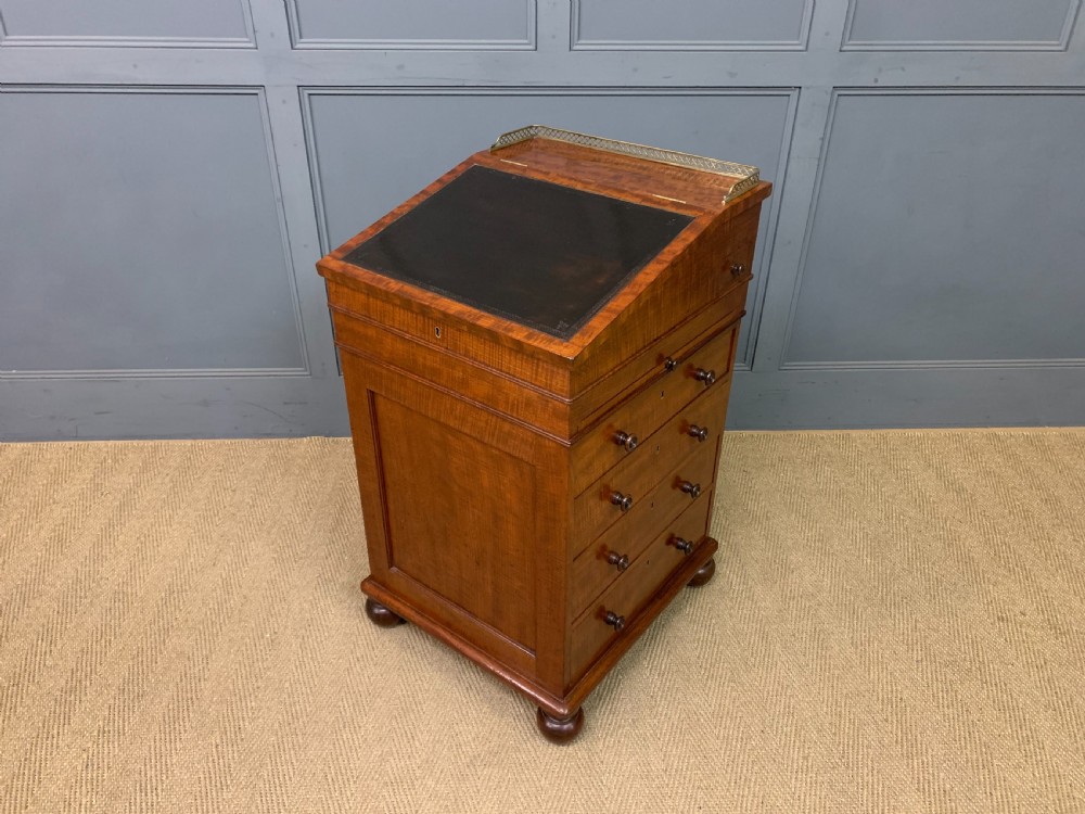 A George IV mahogany Davenport desk featuring a slanted brown leather writing surface, brass gallery rail, four side drawers with turned knobs, and bun feet.