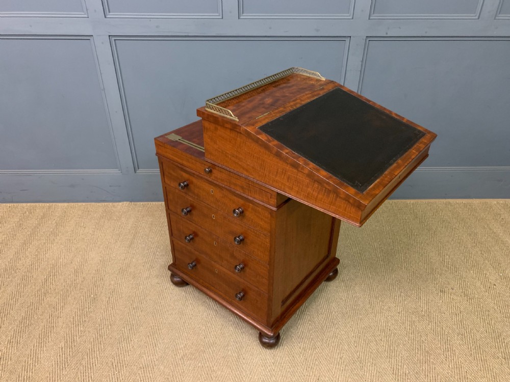 A George IV mahogany Davenport desk featuring a slanted brown leather writing surface, brass gallery rail, four side drawers with turned knobs, and bun feet. View II