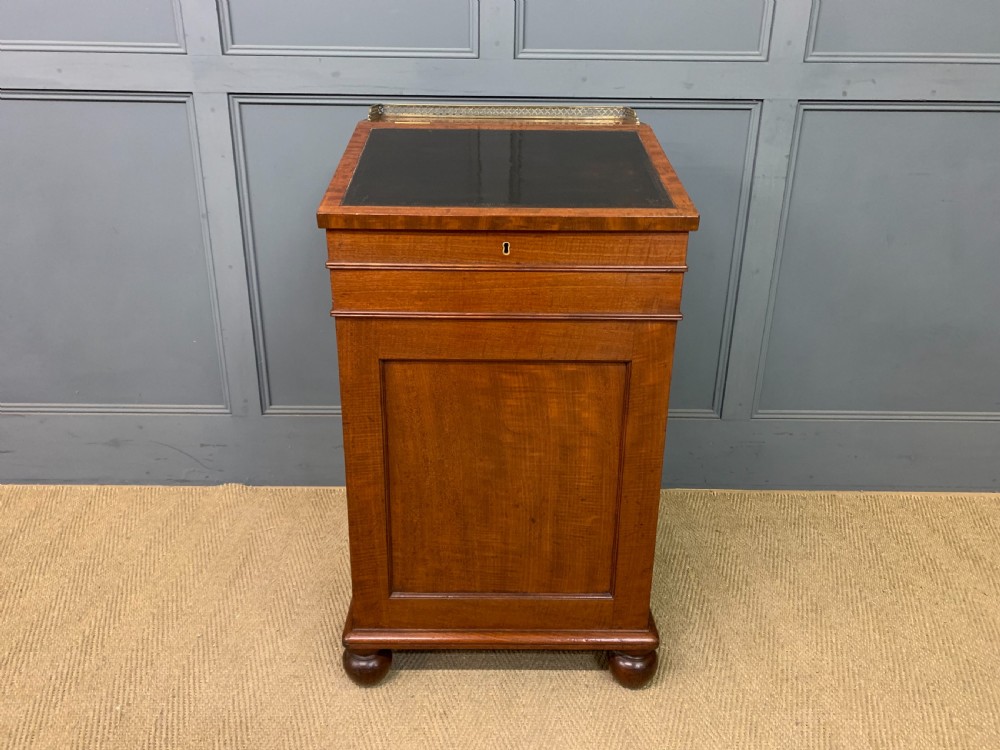 A George IV mahogany Davenport desk featuring a slanted brown leather writing surface, brass gallery rail, four side drawers with turned knobs, and bun feet. View IV